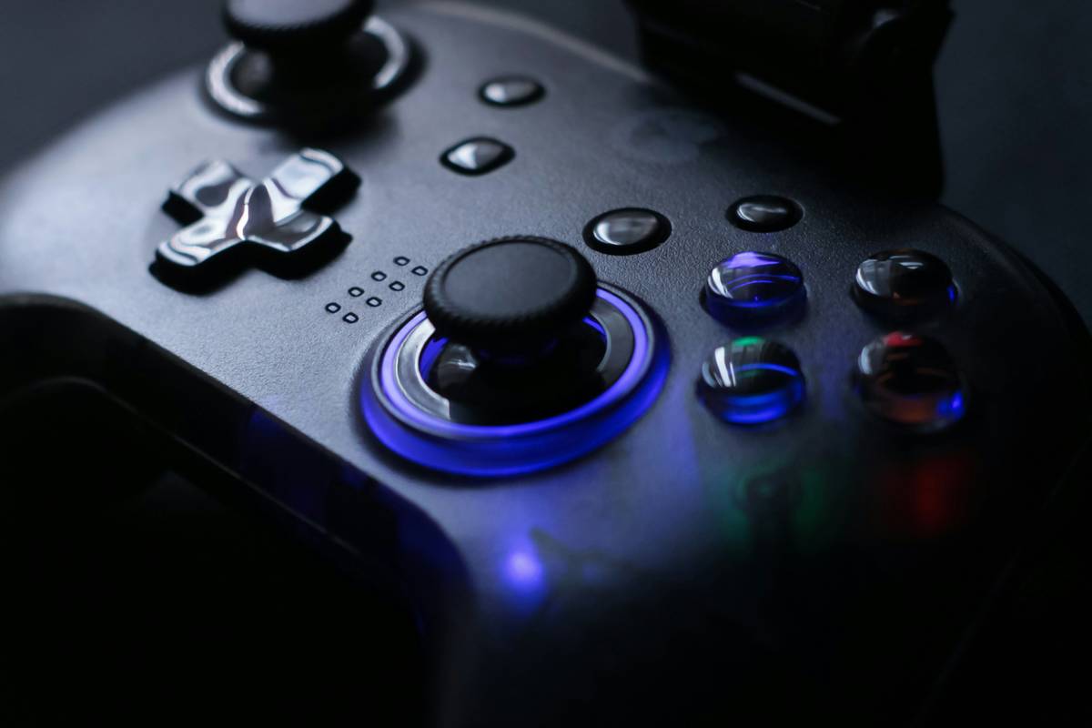 gaming accessory ps4 how to pause: hand holding a DualShock 4 controller with PS button highlighted on a dimly lit gaming desk