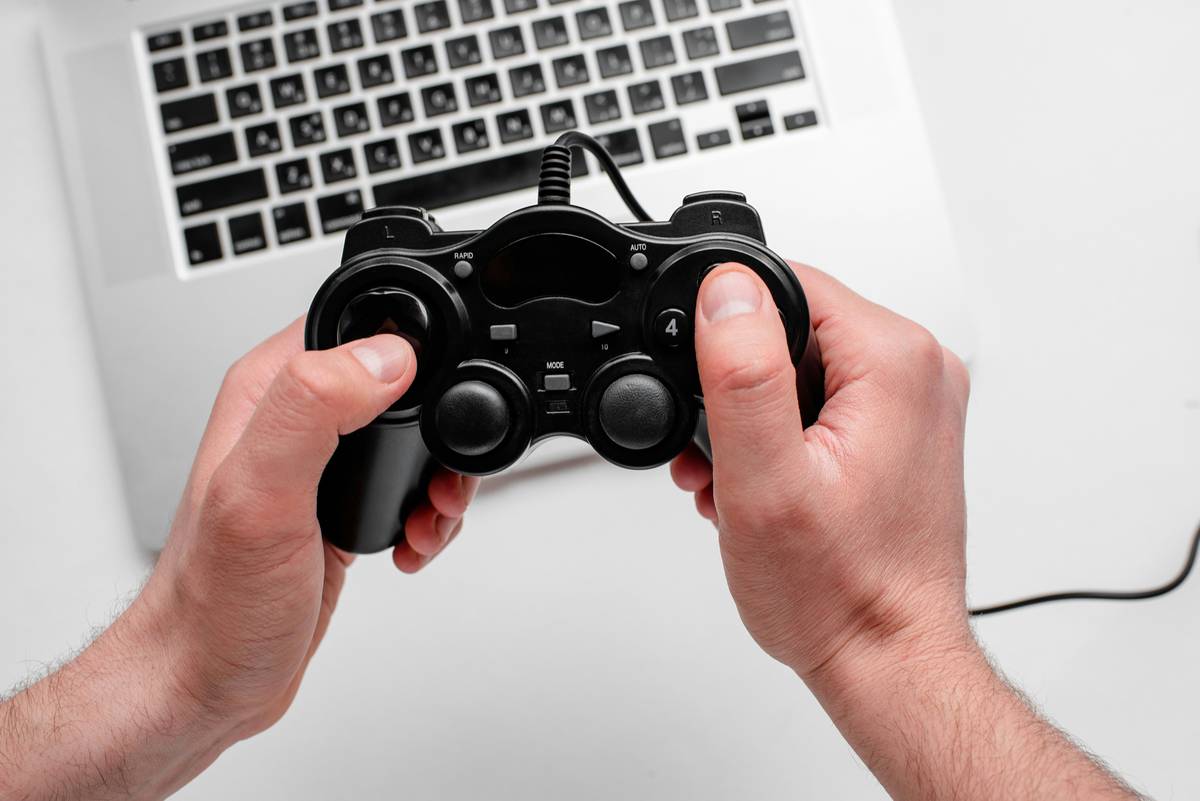 game console ps4 how to use: hand holding a PS4 DualShock 4 controller with USB cable plugged in, showing correct connection method